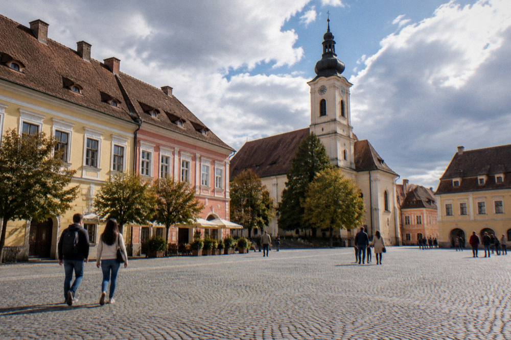 Visitors walking across a large cobbled square ringed by colourful baroque buildings