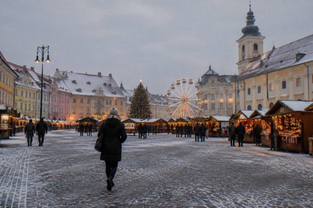 The Christmas market in Piața Mare in Sibiu with wooden stalls and a lit ferris wheel at dusk