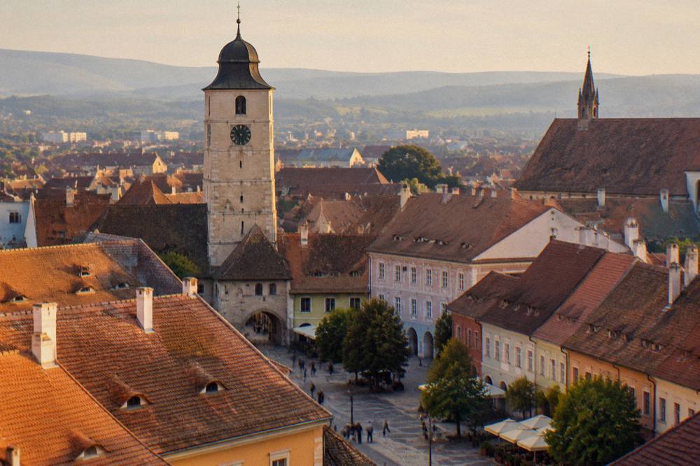 A stone tower and colourful old town rooftops of Sibiu seen from a church tower viewpoint