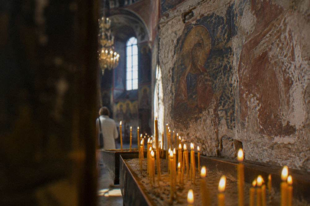 Candles burning in rows of sand before icons inside an Orthodox church