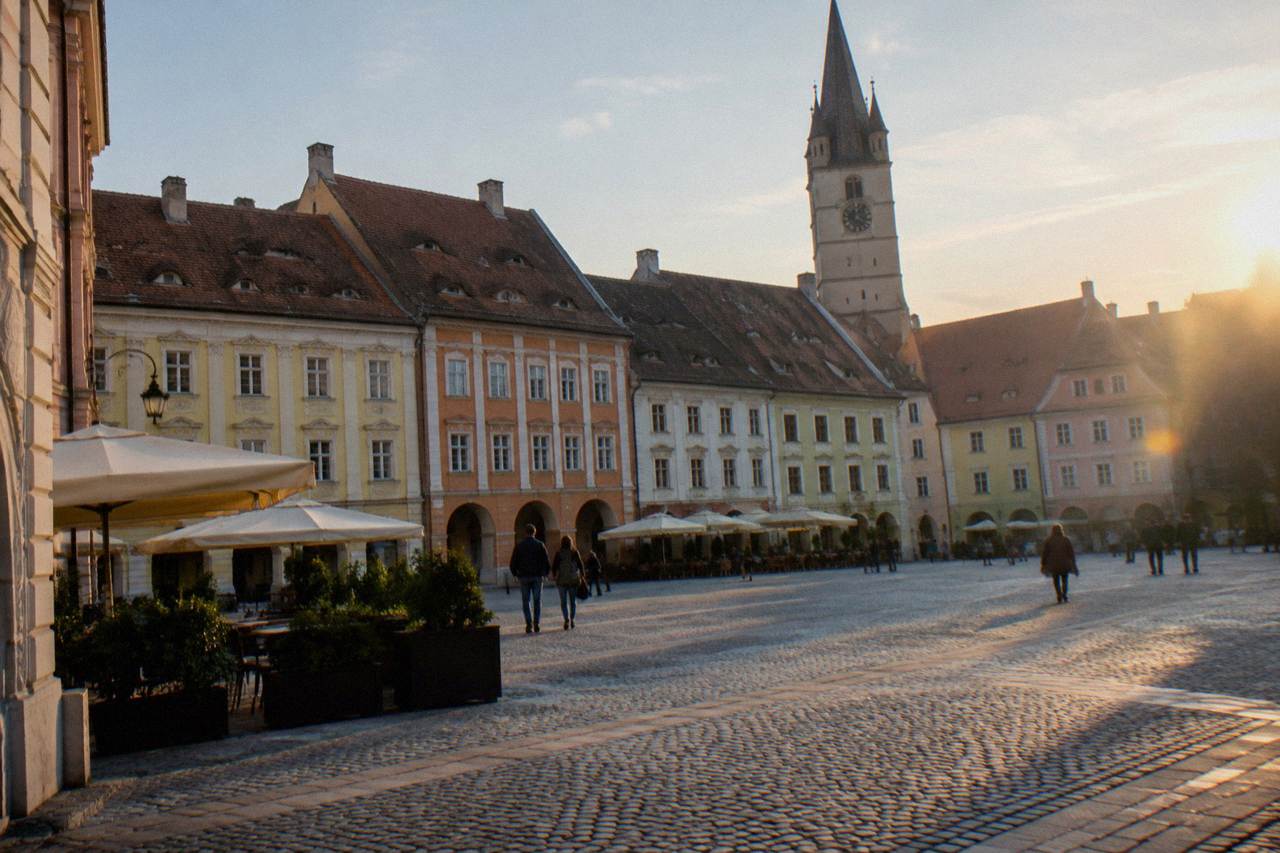 A wide medieval square in Sibiu with colourful baroque facades and a church tower rising behind the rooftops
