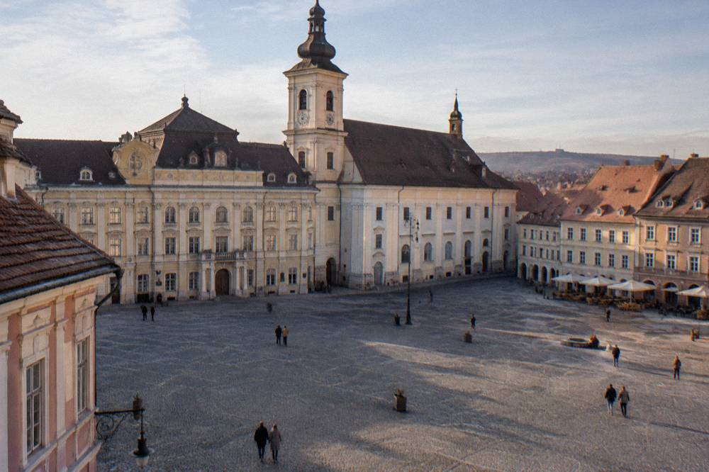A baroque palace facade with arched windows facing a broad square in daylight