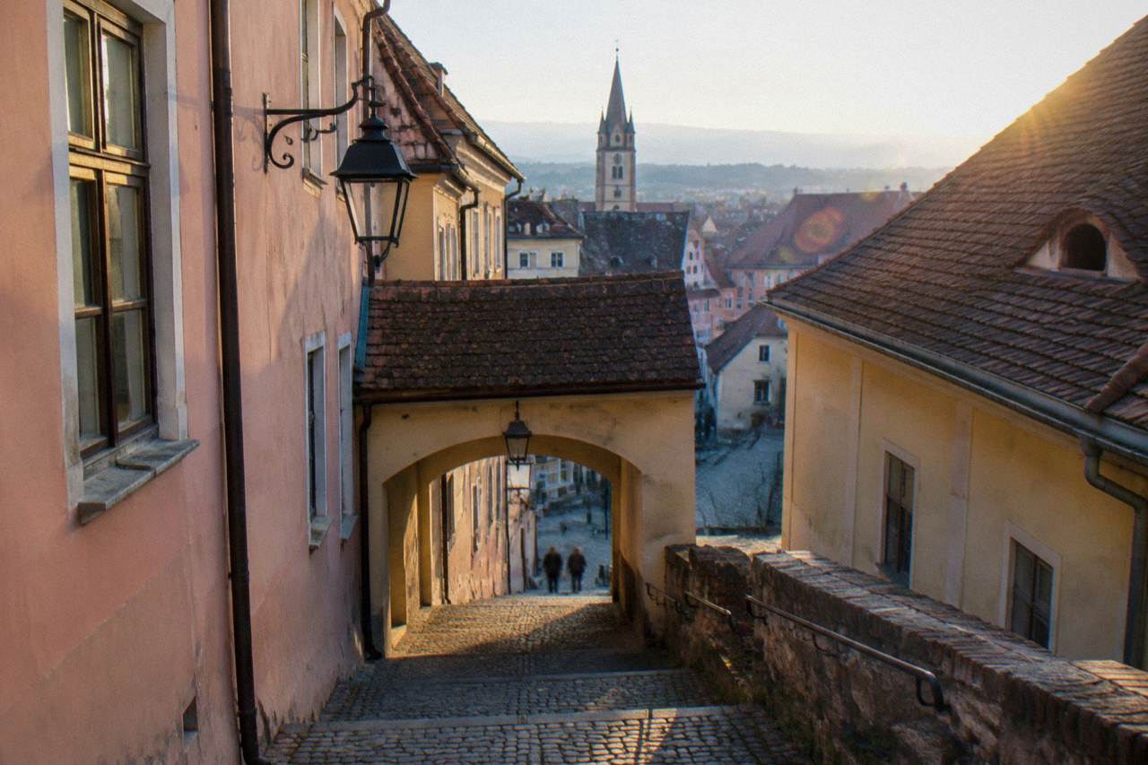 A covered stone staircase rising between pastel-coloured houses in the old town of Sibiu