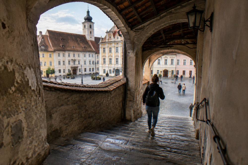 Visitors walking across a broad paved square surrounded by historic facades