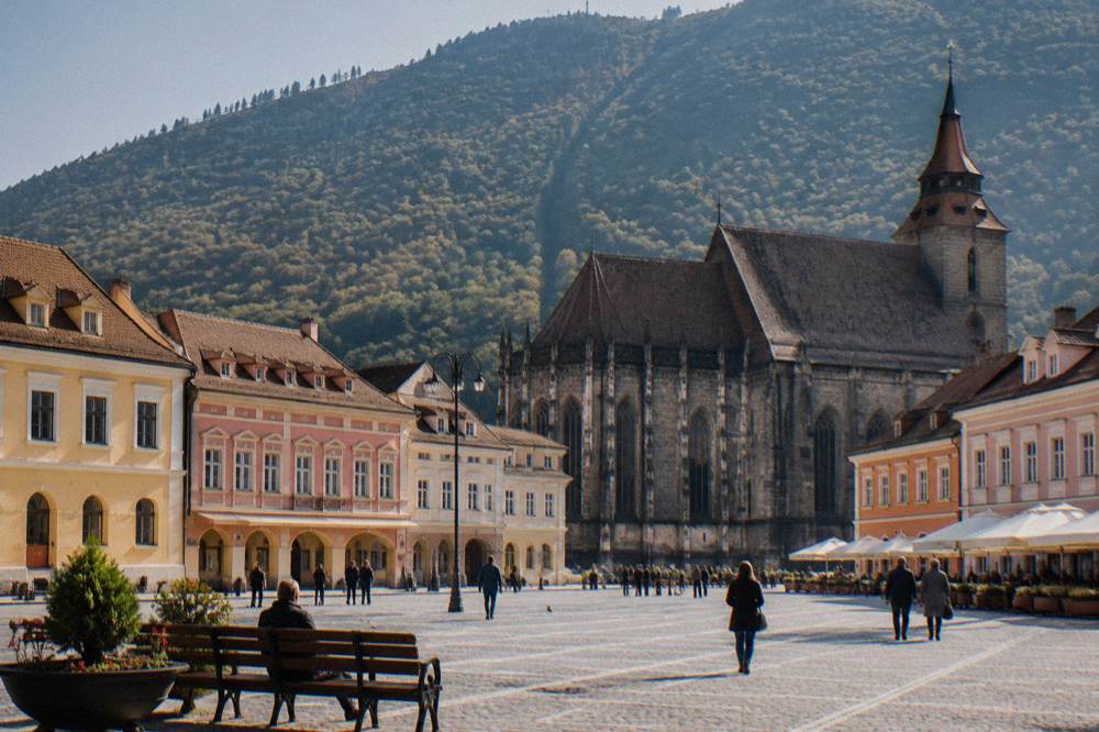 The colourful old town square of Brașov with baroque buildings and the black church tower behind
