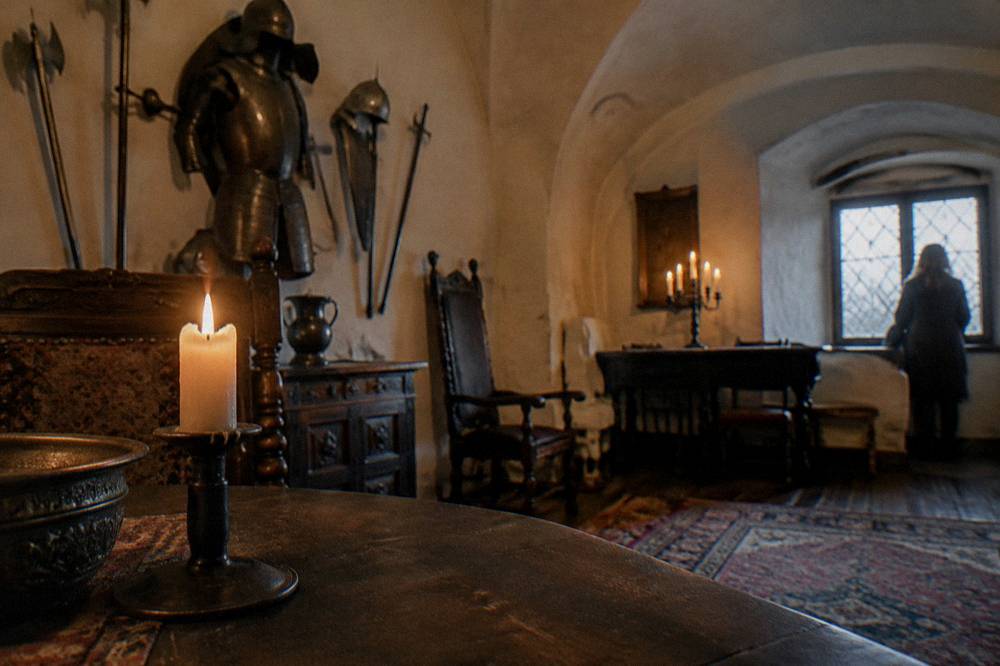A candle-lit stone room in Bran Castle with antique furniture and armour displayed on the wall
