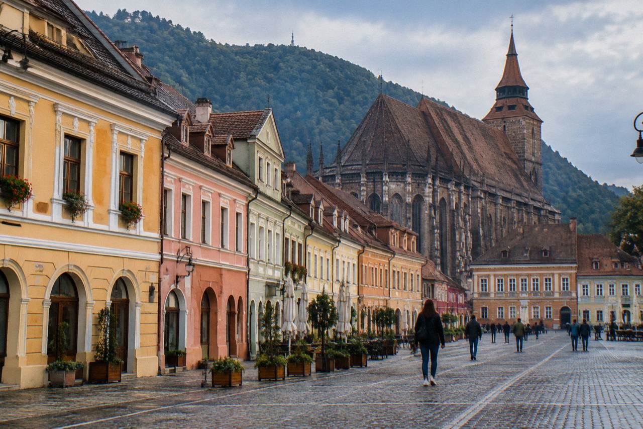 Colourful baroque buildings along a pedestrian street in the old centre of Brașov with the Black Church rising behind them