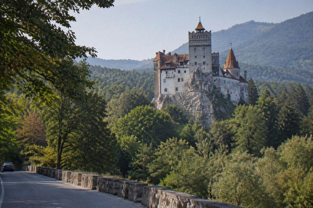 Bran Castle on its rocky hill with wooded slopes behind, seen from the road below