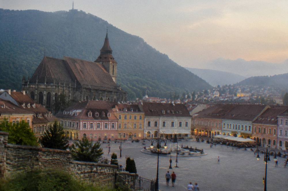 Twilight over a Transylvanian road with distant illuminated town rooftops and dark mountains on the horizon