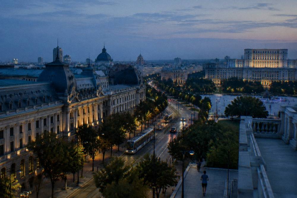 An evening view over Bucharest rooftops with illuminated buildings and a wide horizon