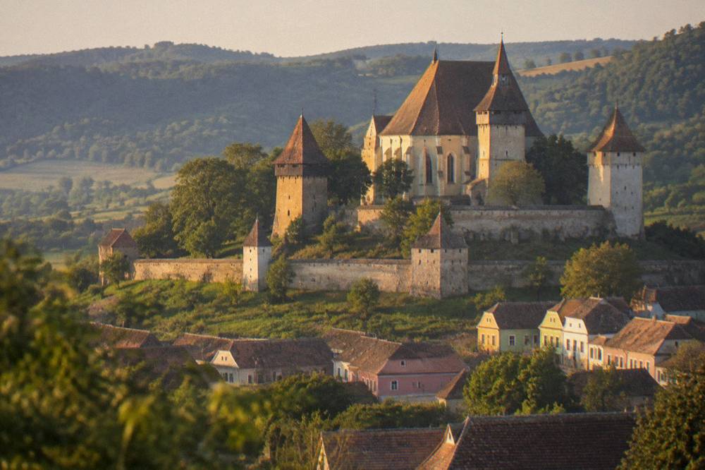 Stone fortified church on a green hill overlooking a small Transylvanian village