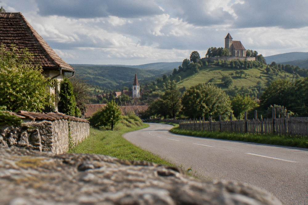 Country road winding between green hills toward a Transylvanian village church