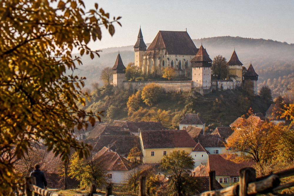 Fortified church walls and towers seen across autumn-coloured trees