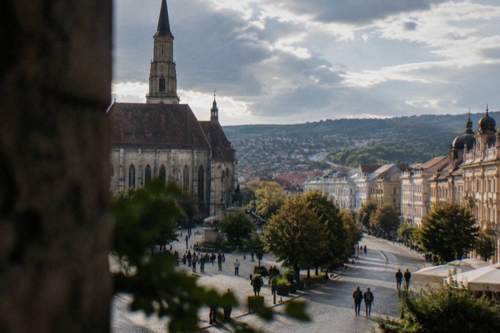 A road winding through green Transylvanian hills with distant town rooftops