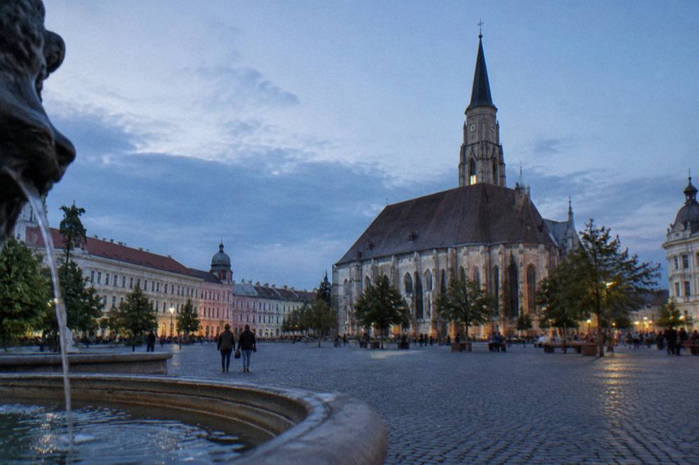 A large cobblestone square in Cluj-Napoca with a gothic church and colourful facades