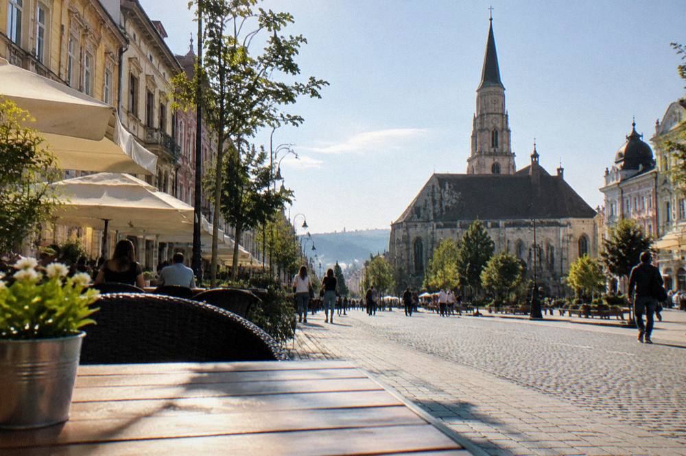 A busy city street in Cluj-Napoca lined with colourful historic buildings and cafes