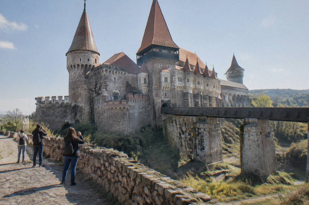 Travellers photographing the towers of Corvin Castle from the moat path