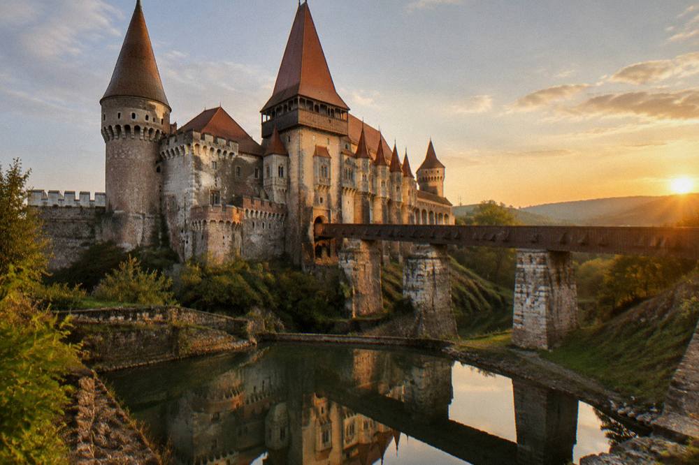Corvin Castle illuminated in the evening with its reflection in the moat