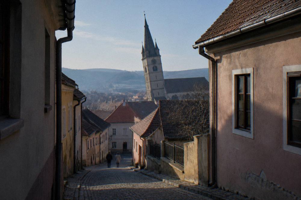 A leaning church tower above red rooftops seen from a narrow street