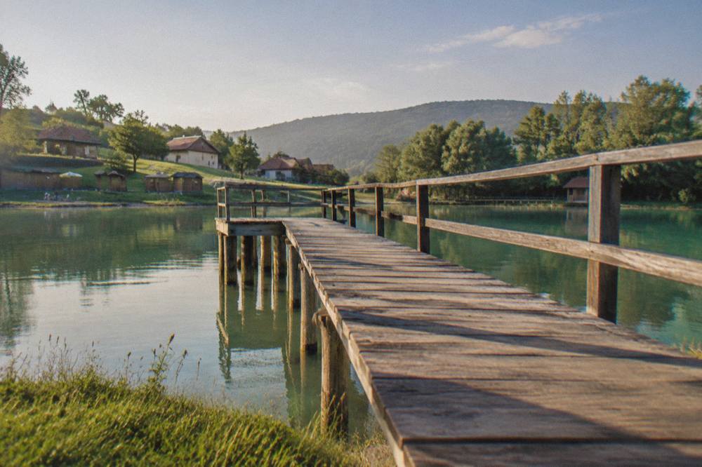 A wooden jetty reaching over a calm green salt lake surrounded by trees