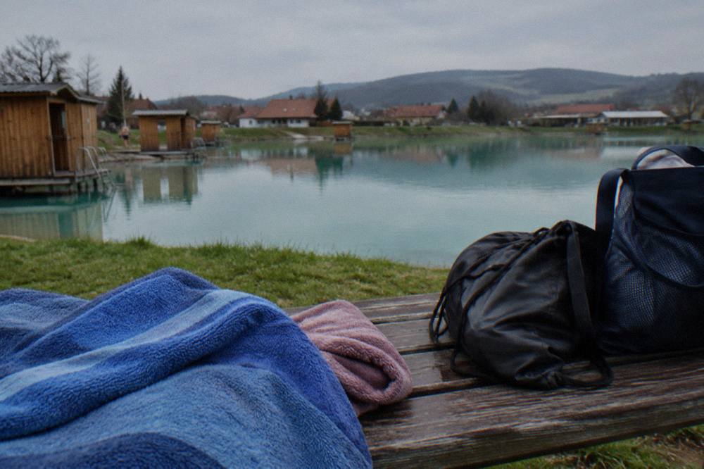 Towels and swim bags on a wooden bench beside a still salt lake