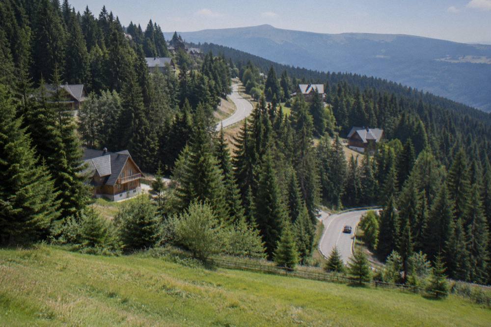A winding mountain road climbing through dense spruce forest toward a resort