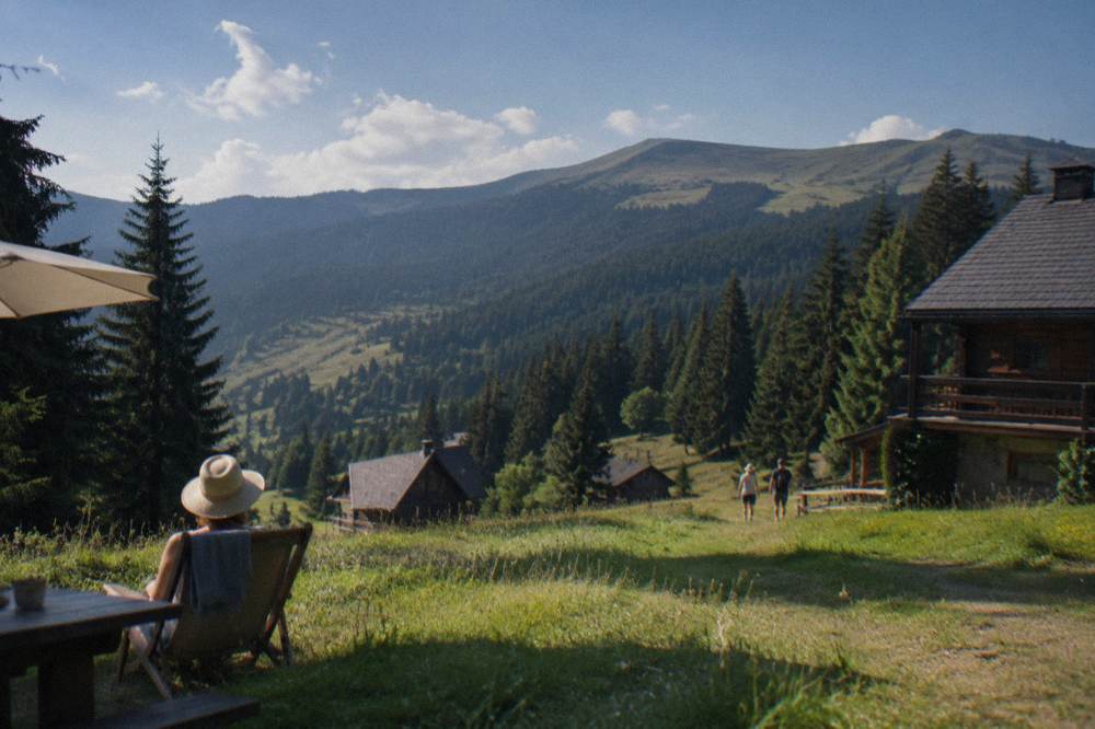 Green alpine meadows with scattered fir trees and a ridge line under summer clouds