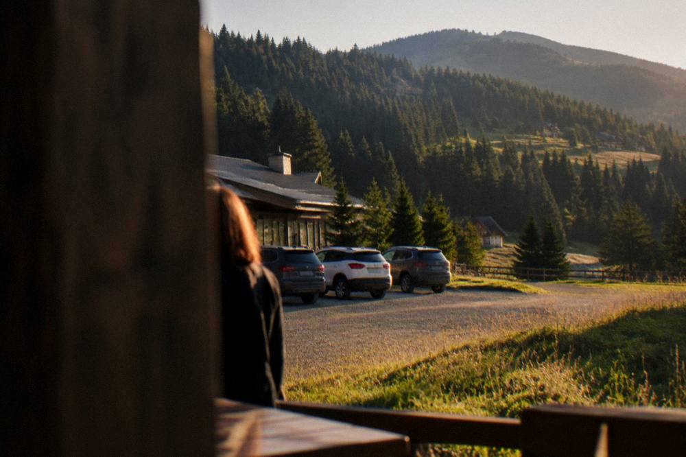 A car park edge at a mountain resort with a low resort building and forest behind