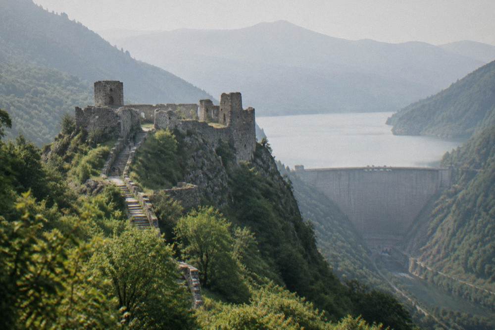 A tall concrete dam wall holding a reservoir between steep forested mountains