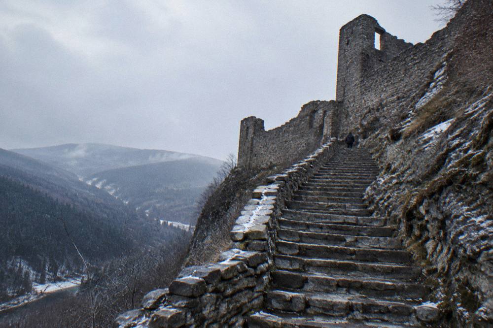 Weathered stone walls of a ruined fortress with open sky above a deep green valley