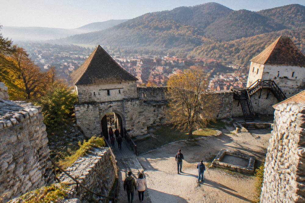 A stone castle gate and courtyard on a forested hillside in autumn light