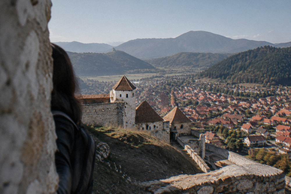 Panoramic view from fortress walls over red rooftops and a valley with forested hills