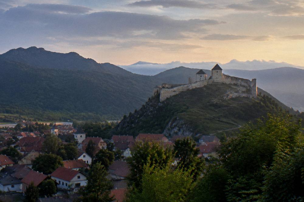Evening light on a fortress silhouette above a valley with distant mountains