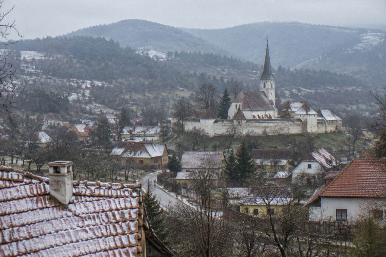 A small Romanian village church with a fortified wall standing among green hills