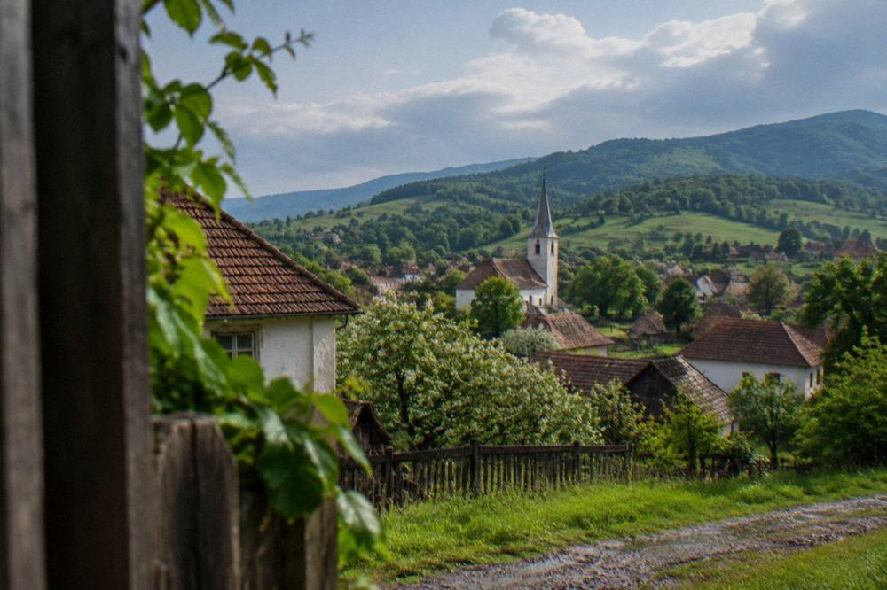 Rolling green hills with scattered farms under a partly cloudy sky in Mărginimea Sibiului