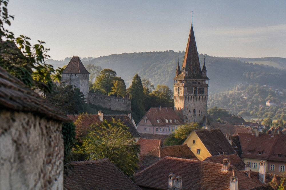 The clock tower of Sighișoara rising above red tiled rooftops seen from the citadel hill