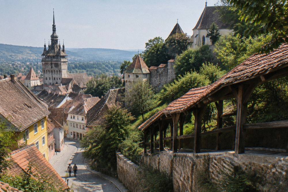 A covered wooden staircase with a red tiled roof climbing the hillside toward a church in Sighișoara