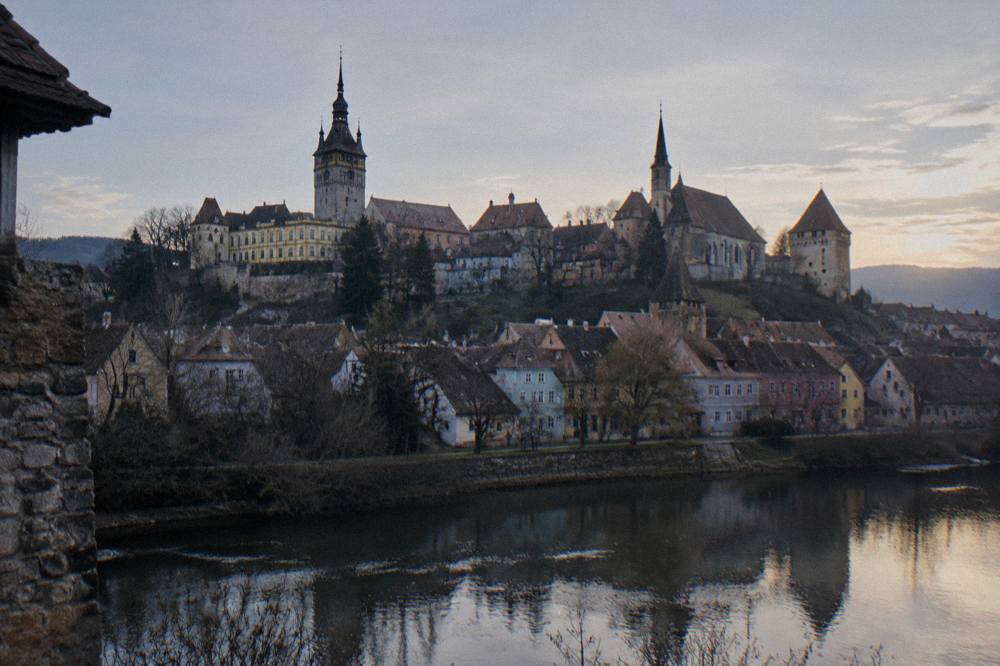 The walled skyline of Sighișoara citadel with church spires and towers seen from across the river at dusk