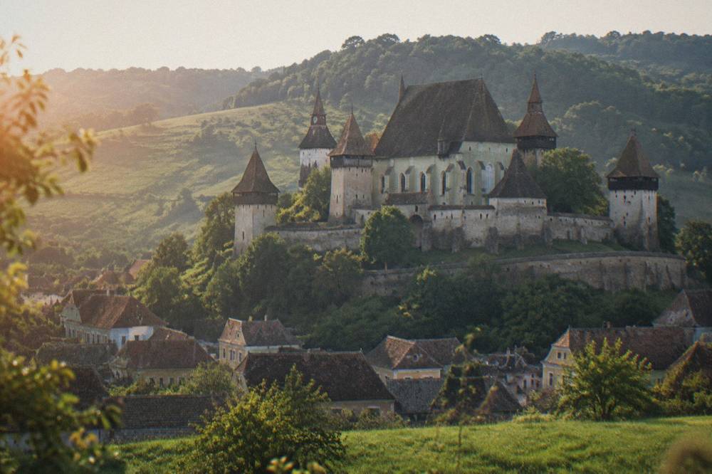 A fortified church with high defensive walls surrounded by green village fields