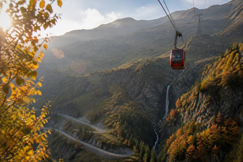 A cable car ascending above a waterfall toward mountain tops