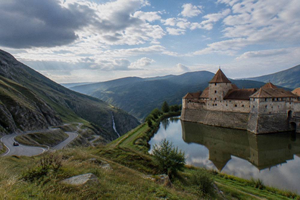 A medieval fortress reflected in a moat seen from a grassy bank
