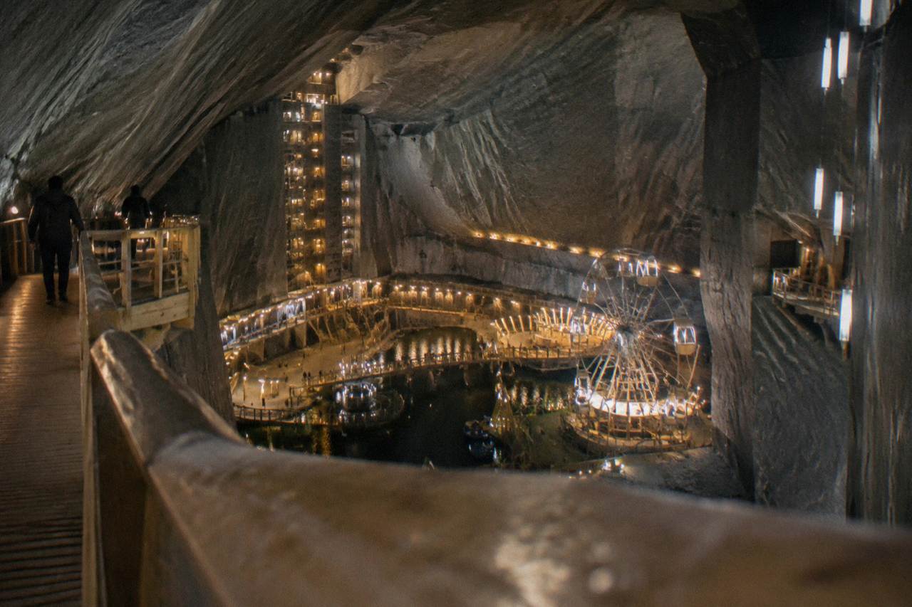 The vast underground chamber of a salt mine lit in warm colors, with a ferris wheel and balconies carved into the rock walls