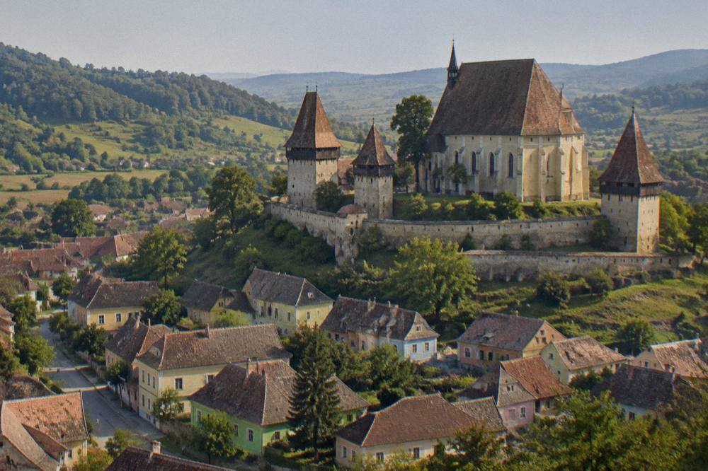 A fortified church with high walls and towers standing above a village of red roofs