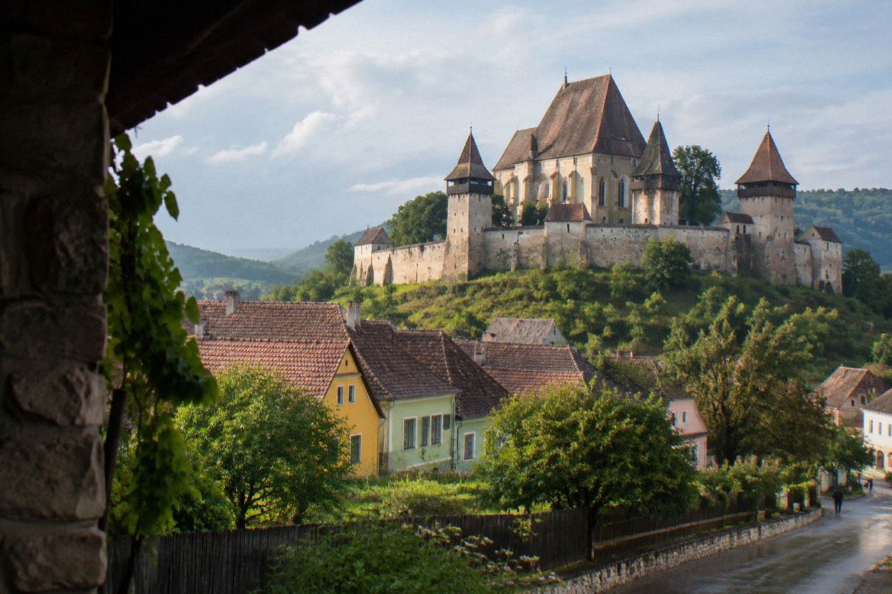 A fortified church with tall defensive walls rising behind village houses in a Transylvanian valley