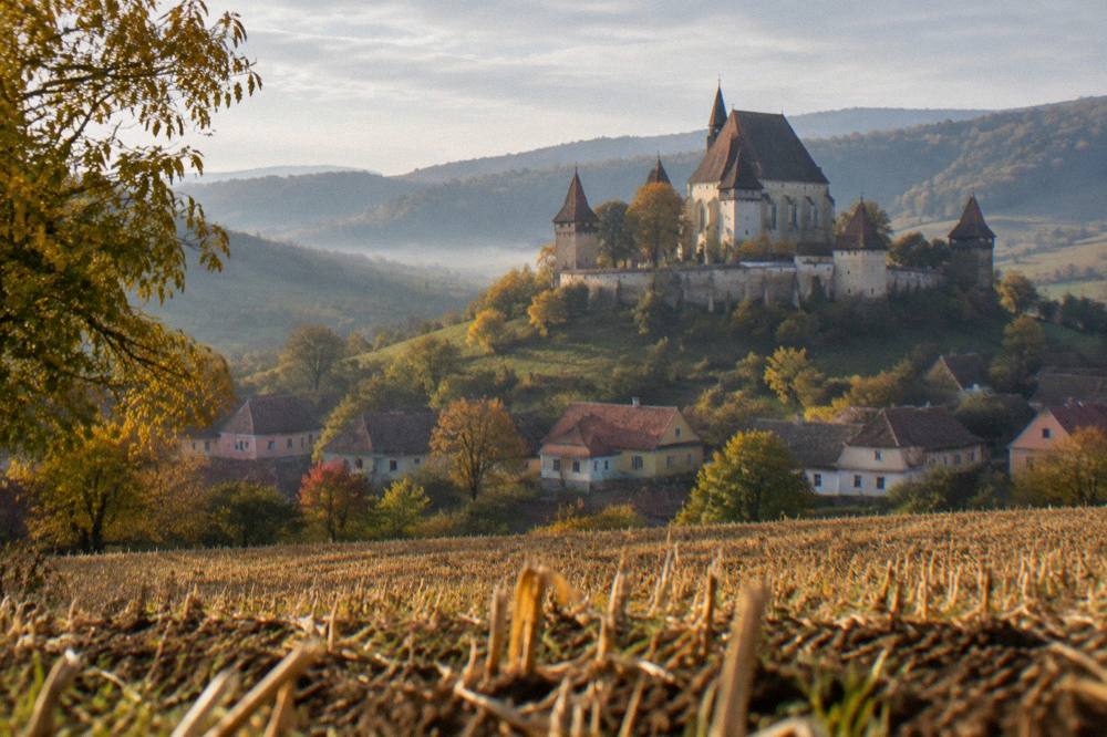 A fortified church tower seen across golden harvested fields in early autumn