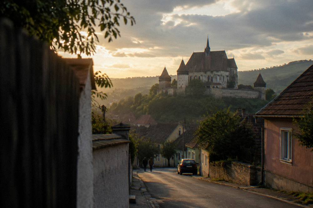 Evening light over a Transylvanian village street with the fortified church silhouette in the distance