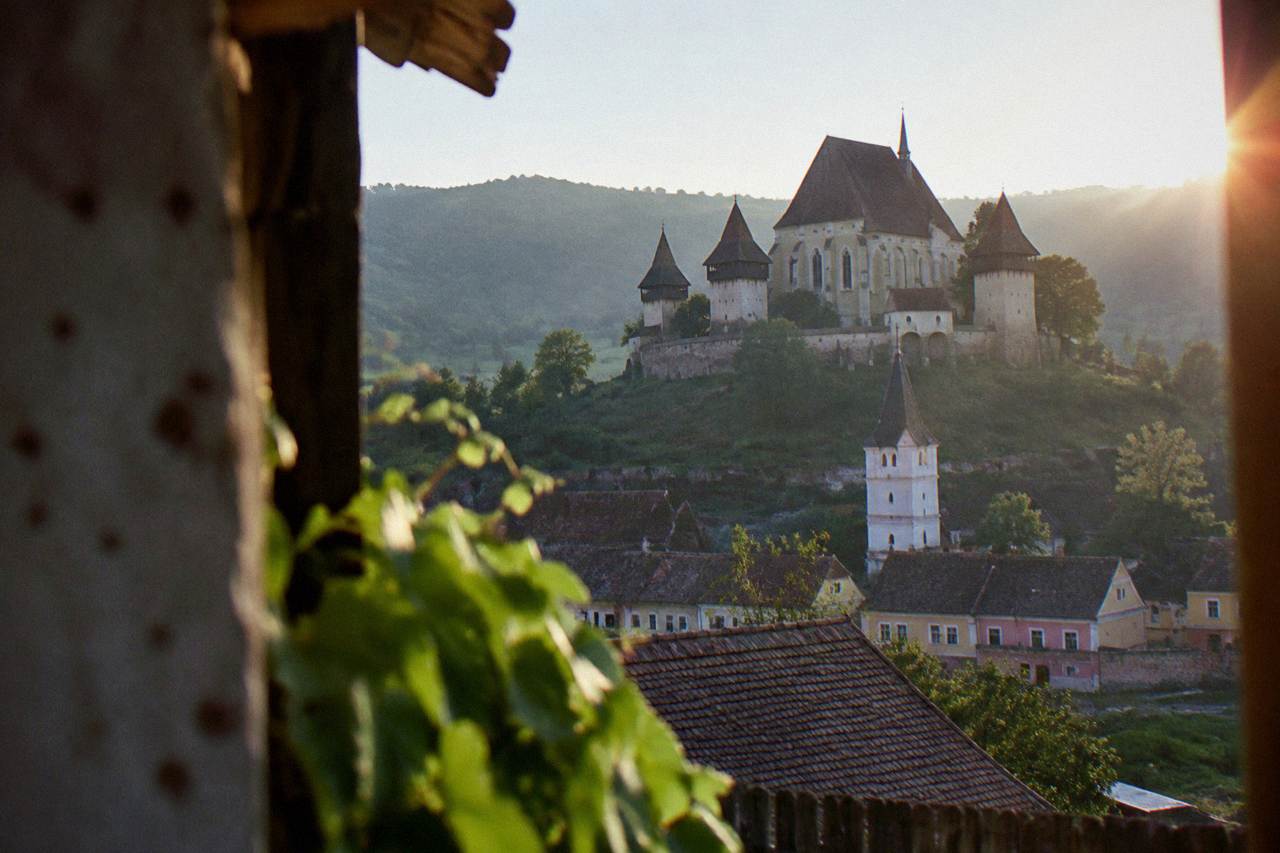 A small fortified church with a white tower standing above village houses and green hills