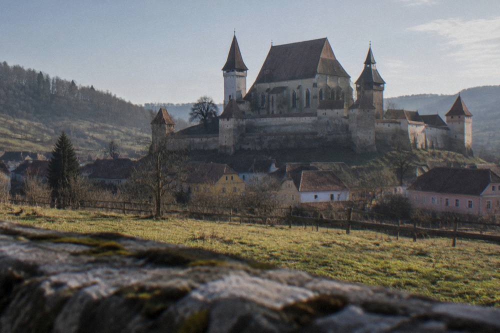 A large fortified church complex with twin towers and high defensive walls seen across a meadow