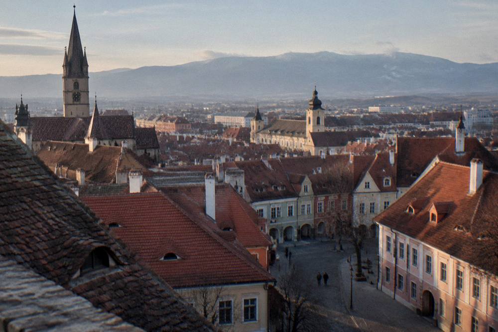 View over the red rooftops of Sibiu toward distant mountains in soft evening light