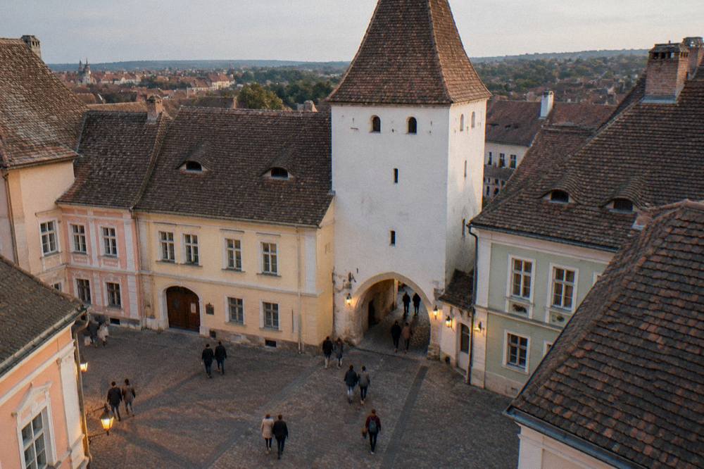 Pedestrians crossing a cobbled square in front of the Council Tower in Sibiu